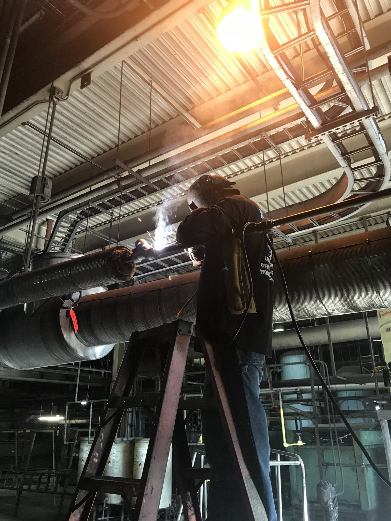 McPherson Specialty Welding welder arc-welding overhead pipe at an industrial plant